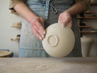 Unrecognizable woman ceramist peeling a clay plate holding sponge. The process of irregularities and grinding of the finished product. Small business, hobby, ceramic concept. - obrazy, fototapety, plakaty