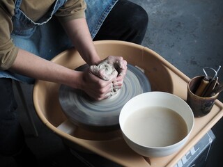 Young female master working on a potter’s wheel, creates clay dishes. Ceramist young woman making clay product on pottery wheel in her cozy studio. Small business, art, hobby, handcraft concept.