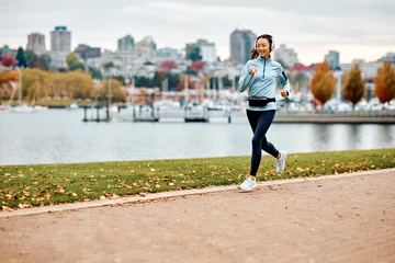 Poster Happy Asian female runner with headphones jogging outdoors. © Drazen