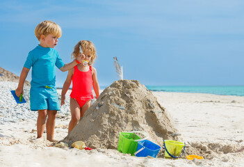 Boy and girl build sand castle putting feather on top at a beach