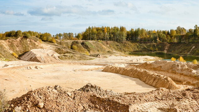 a sand quarry, in the photo a quarry against a background of blue sky and clouds also in the background trees shrubs and forest