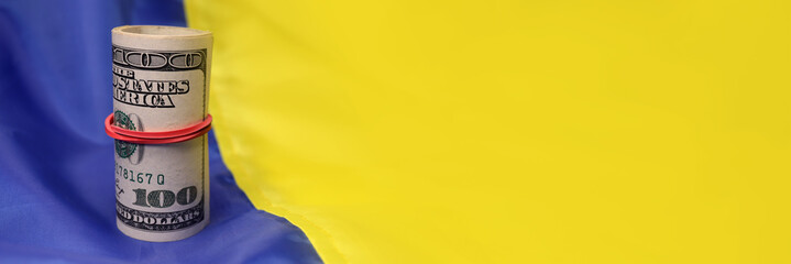 Roll of dollars on the Ukrainian flag. The concept of lend lease, war in Ukraine, financial donations, aid. Horizontal banner. copy space for text