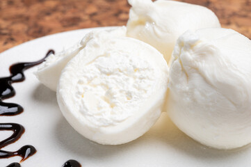 Eating of fresh handmade soft Italian cheese from Puglia, white balls of burrata or burratina cheese made from mozzarella and cream filling served with balsamico cream