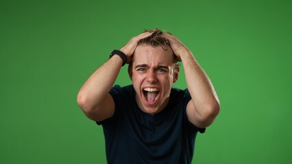 Yelling angry frustrated despair upset with clenched fists portrait of young man 20s isolated isolated on green screen background in slow motion