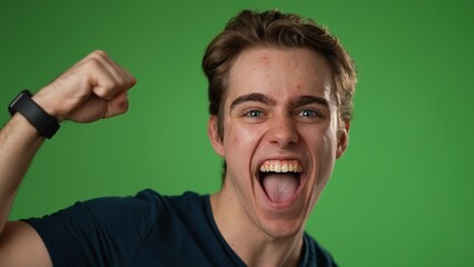 Closeup slow motion of excited jubilant overjoyed young man 20s doing winner gesture celebrate clenching fists say yes isolated on green screen background studio portrait