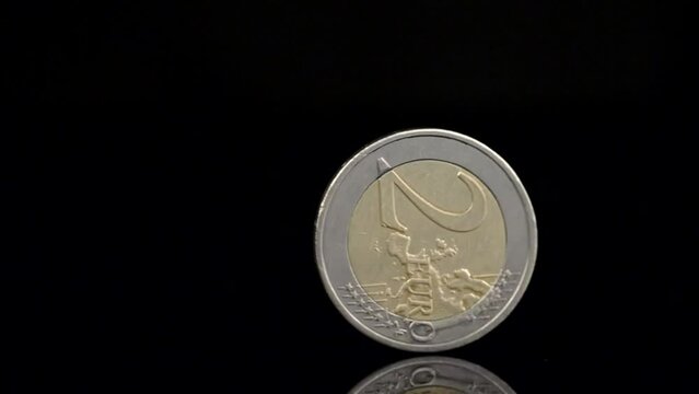 Two Euro coin spinning on black background. Falling or rising euro currency. Close up slow motion shot
