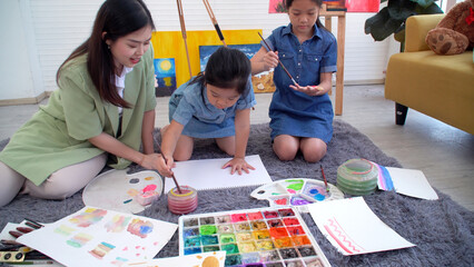 Asian two siblings learning study watercolor paint hand together at home. Teacher or parent teach student or daughter use hand paint color imagination on paper homework.Activity creativity education