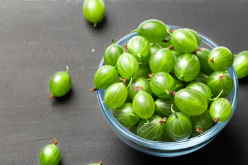 Ripe green gooseberries in a glass transparent bowl and jar on a black  background. Harvest concept agrus. Vegetarian food.Top view