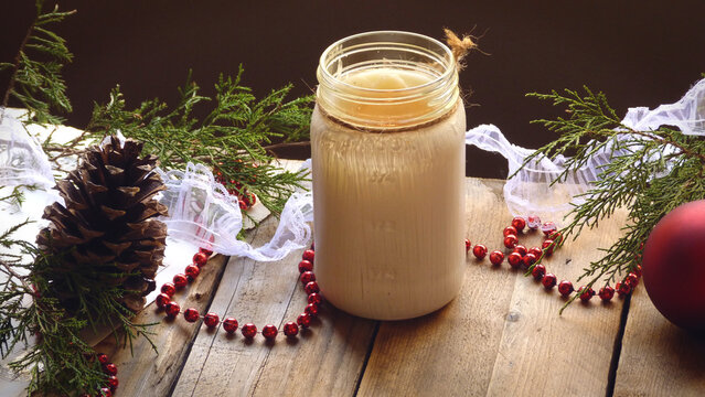 A Rustic Candle with an Ornament, Pine Cone, Beads, Lace, and Evergreen Boughs on a Wooden Background | Christmas Decorations | Christmas Candle