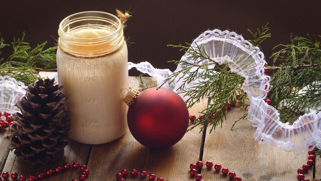 A Rustic Candle with an Ornament, Pine Cone, Beads, Lace, and Evergreen Boughs on a Wooden Background | Christmas Decorations | Christmas Candle