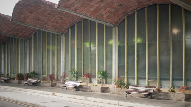 Bancos de madera junto a pabell&oacute;n de hormig&oacute;n verde y cristaleras