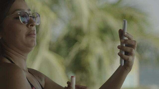Close up of woman holding cell phone and applying lipstick / El Tunco, La Libertad, El Salvador