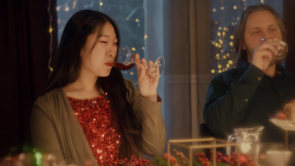 Friends clink glasses, drinking wine and talking. Multi cultural friends celebrating Christmas or New Year 2023. Served holiday table. Warm atmosphere of Christmas dinner at home. Christmas party.