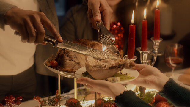 Close-up Shot Of African American Man Cutting Turkey Or Chicken. Multi Cultural Family Celebrating Christmas Or Thanksgiving Day. Served Table With Dishes And Candles. Family Christmas Dinner At Home.