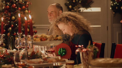 Happy multi cultural family celebrating Christmas or New Year 2023, exchanging gifts. Served holiday table with different dishes and candles. Warm atmosphere of family Christmas dinner at home.