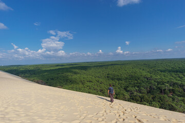 Fototapeta premium Tourist standing on Dune du Pilat, the biggest sand dune in Europe with the pine forest and view at the sea, Arcachon, Nouvelle-Aquitaine, France