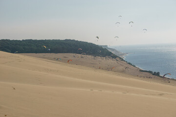 Many paragliders flying in the windy air over the dune of Pilat on a sunny day, Arcachon,...