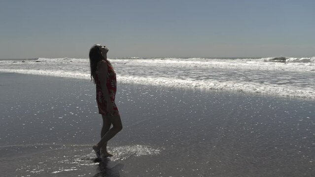 Tracking shot of woman walking in waves on ocean beach / San Blas, La Libertad, El Salvador