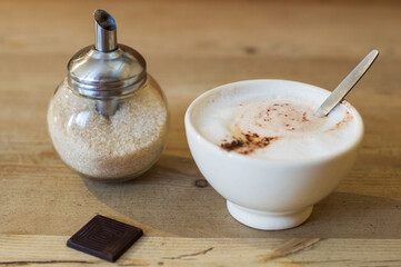 a cup of cappuccino and a sugar bowl with a dispenser on a table in a cafe
