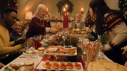 Happy large family sitting at table and celebrating Christmas or New Year at home. Grandmother set the table with traditional dish turkey. Warm atmosphere of family Christmas dinner. Christmas Eve.