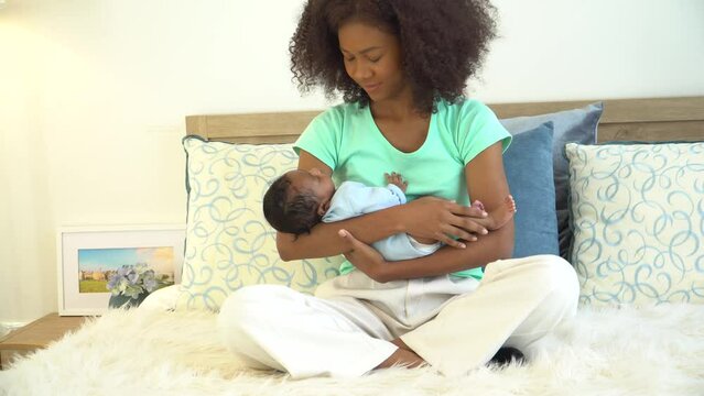 Young mother African American holding her one-month-old newborn baby son carefully and gently in bedroom. Adorable little infant sleep well in warm embrace of motherhood. Happy mother's day concept