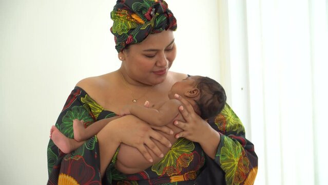 Portrait Asian mother in traditional dress clothing native-style African carry newborn baby one-month-old breastfeeding. Happy infant mixed race afro-Asia sleep well in warm embrace of motherhood.