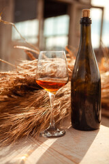 a glass of amber wine and a bottle of wine near a sheaf of wheat
