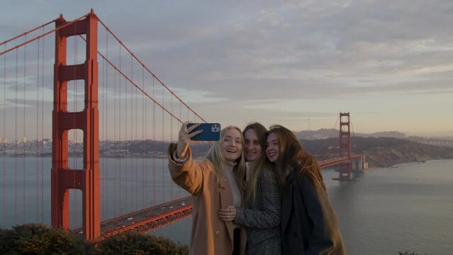 Portrait of young women posing for selfie photo with iconic American landmark behind. Pretty, caucasian girls in their 20s enjoying cinematic sunset over Bay Area in SF city. High quality 4k footage