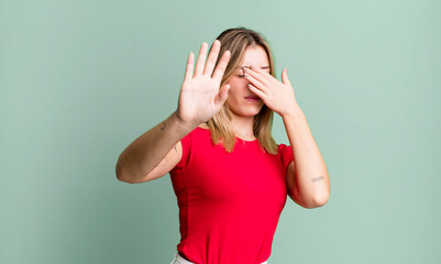 blonde pretty woman covering face with hand and putting other hand up front to stop camera,...