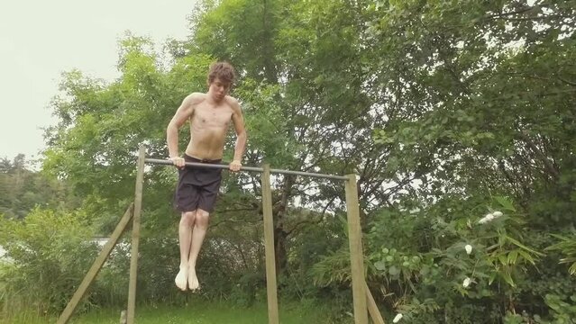 Young man exercises by doing muscle-up pullups outdoors on home gym