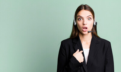 young pretty woman looking shocked and surprised with mouth wide open, pointing to self. telemarketing agent concept