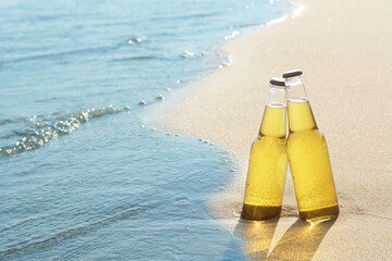 Bottles of cold beer on sandy beach near sea, space for text