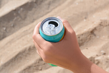 Woman holding aluminum can with beverage on sand, closeup