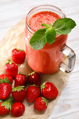 Mason jar of tasty smoothie and fresh strawberries on white wooden table, above view