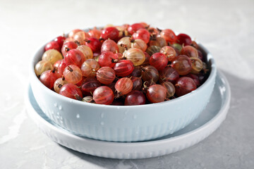 Bowl full of ripe gooseberries on light grey marble table, closeup