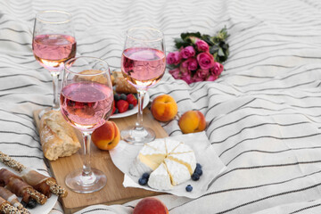 Glasses of delicious rose wine, flowers and food on white picnic blanket