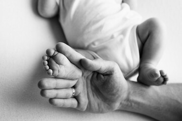 Baby feet in the hands of mother, father, older brother or sister, family. Feet of a tiny newborn close up. Little children's feet surrounded by the palms of the family. Black and white.
