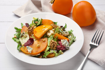 Delicious persimmon salad and fork on white wooden table