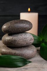 Stacked spa stones with bamboo leaves and candle on wooden table, closeup