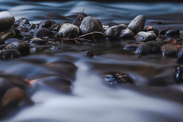 tranquil misty stream flowing through smooth natural rocks, pebbles and sticks.