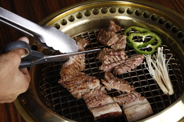 Grilled beef for korean samgyeopsal meal with hands cutting it to bite-sized pieces