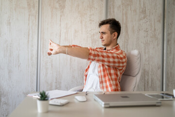 young man stretching at work while sitting at desk having back pain