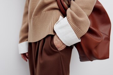 a gentle beautiful woman is standing sideways on a light background in a sweater and shirt, wearing a bag on one shoulder and putting her hand in her pocket, The subject is close shooting