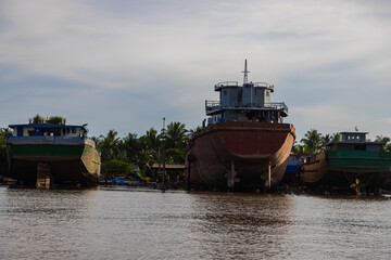 Ho Chi Minh City, Vietnam- November 9, 2022: The River Bank of the Mekong river at sunset. Last sun beams touching the old rusty cargo ships on the pier. Mode of transportation at the Mekong Delta