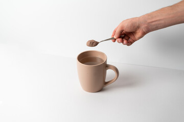 hand holds a spoon with cocoa powder and put it in cup with hot water