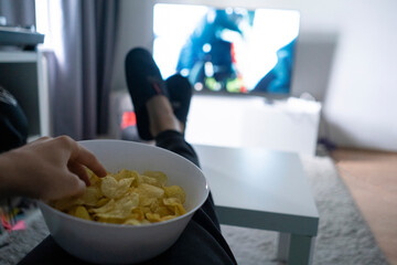 person holding large bowl with potato chips and watching series on tv
