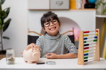 Obraz na płótnie Canvas Little Asian girl saving money in a piggy bank, learning about saving, Kid save money for future education. Money, finances, insurance, and people concept