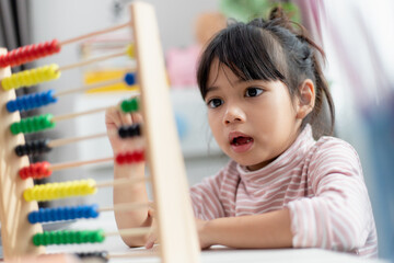A young cute Asian girl is using the abacus with colored beads to learn how to count at home