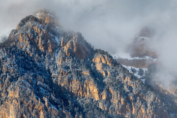 Fototapeta na wymiar Skalisty Mountain Range in the clouds on sunny winter day. Digoria, North Ossetia, Russia.