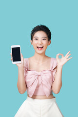 Cheerful Asian woman holding smartphone and shows ok sign on light cyan background.